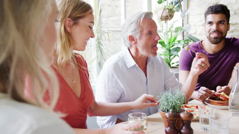 Vier-Erwachsene-Freunde-Gemischten-Alters-Reden-Und-Essen-Gemeinsam-An-Einem-Tisch-Zu-Mittag,-Selektiver-Fokus
