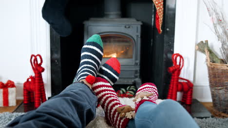 Nahaufnahme-Eines-älteren-Paares,-Das-Weihnachtssocken-Trägt-Und-Die-Füße-Am-Holzofen-Wärmt