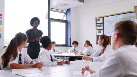 Weibliche-Nachhilfelehrerin-Unterrichtet-Eine-Gruppe-Von-Schülern-In-Uniform,-Die-An-Tischen-Im-Klassenzimmer-Arbeiten