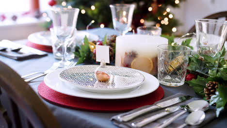 A-festive-Christmas-dining-table-with-bauble-name-card-holder-arranged-on-a-plate-and-green-and-red-seasonal-decorations,-detail