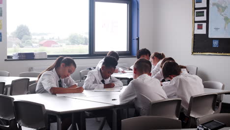 Group-Of-High-School-Students-Wearing-Uniform-Working-At-Desks-In-Classroom