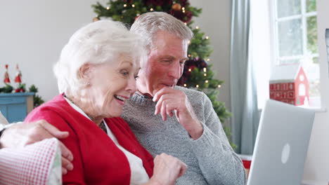 Senior-Couple-Making-Christmas-Video-Call-To-Family-On-Laptop