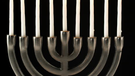 Tilt-shot-of-Jewish-menorah-candelabrum-with-lit-candles-against-black-background