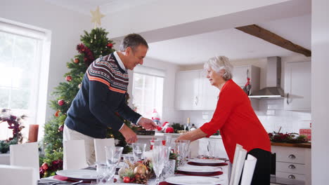 Älteres-Paar-Deckt-Den-Tisch,-Während-Es-Sich-Zu-Hause-Auf-Das-Weihnachtsessen-Der-Familie-Vorbereitet