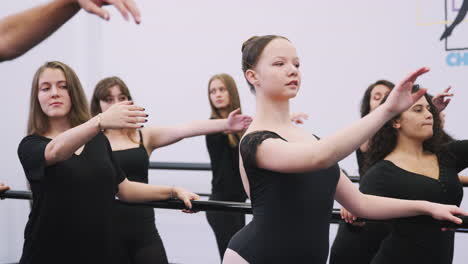 Female-Students-At-Performing-Arts-School-Rehearsing-Ballet-In-Dance-Studio-Using-Barre