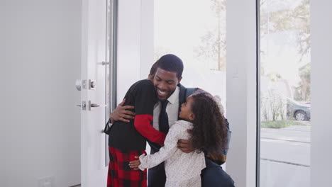 Children-Wearing-Pajamas-Greeting-And-Hugging-Working-Businessman-Father-As-He-Returns-Home-From-Work