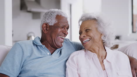 Portrait-Of-Loving-Senior-Couple-Sitting-On-Sofa-At-Home-Laughing-Together