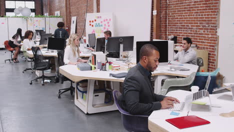 Crane-Shot-Of-Business-Team-Working-At-Desks-In-Modern-Open-Plan-Office