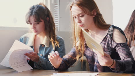 Two-Female-College-Students-Sitting-At-Desk-Using-Digital-Tablet-In-Classroom