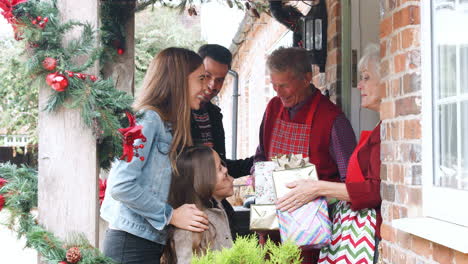 Family-Being-Greeted-By-Grandparents-As-They-Arrive-For-Visit-On-Christmas-Day-With-Gifts