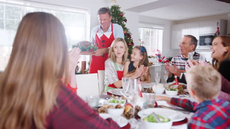 Man-Serving-Turkey-As-Multi-Generation-Family-Sit-Around-Table-For-Christmas-Meal-At-Home-Together