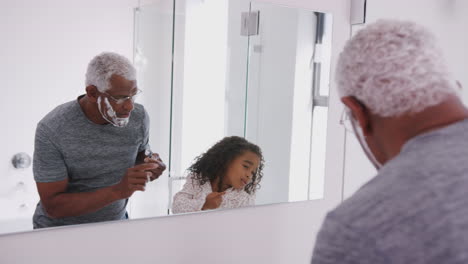 Grandfather-Wearing-Pajamas-In-Bathroom-Shaving-Whilst-Granddaughter-Watches