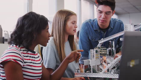 Teacher-With-Two-Female-College-Students-Building-Machine-In-Science-Robotics-Or-Engineering-Class