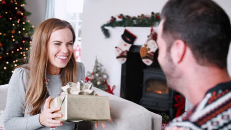 Excited-Woman-Receiving-Christmas-Gift-From-Man-At-Home