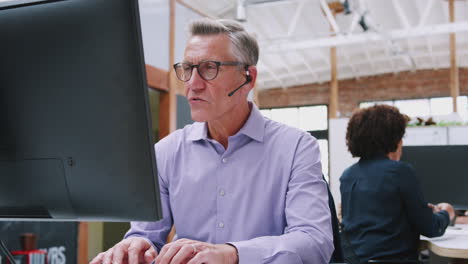 Mature-Male-Customer-Services-Agent-Working-At-Desk-In-Call-Center