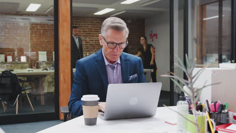 Businessman-And-Businesswoman-Working-On-Computers-In-Open-Plan-Office-With-Colleagues-In-Background