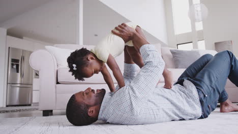 Father-Playing-With-Baby-Daughter-Lifting-Her-In-The-Air-At-Home