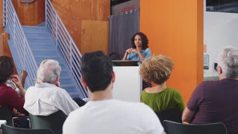 Woman-At-Podium-Chairing-Neighborhood-Meeting-In-Community-Centre