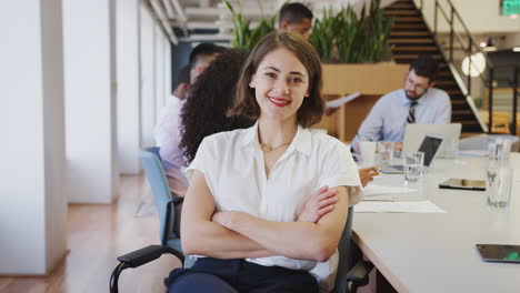 Portrait-Of-Businesswoman-In-Modern-Office-With-Colleagues-Meeting-Around-Table-In-Background