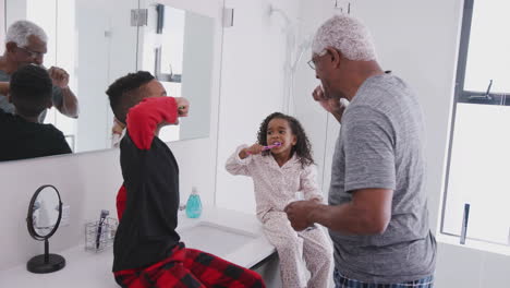 Grandfather-In-Bathroom-Wearing-Pajamas-Helping-Grandchildren-To-Brush-Teeth