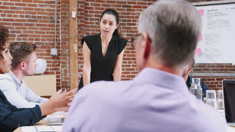 Young-Businesswoman-Standing-And-Leading-Office-Meeting-Around-Table