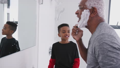 Grandfather-Wearing-Pajamas-In-Bathroom-Shaving-Whilst-Grandson-Watches