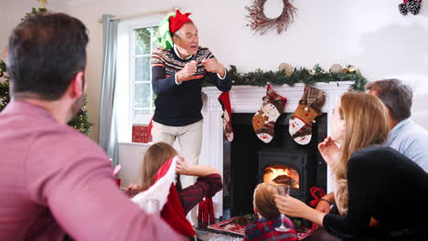 Großvater-Spielt-Pantomime,-Während-Eine-Familie-Aus-Mehreren-Generationen-Zu-Hause-Gemeinsam-Weihnachtsscharaden-Spielt
