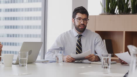 Businessman-With-Paperwork-Sitting-At-Table-Meeting-With-Colleagues-In-Modern-Office