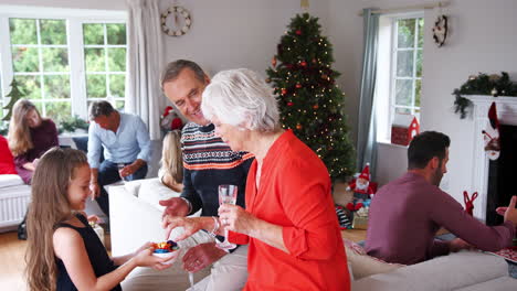 Enkelin-Serviert-Den-Großeltern-Süßigkeiten,-Während-Familie-Und-Freunde-Aus-Mehreren-Generationen-Auf-Der-Weihnachtshausparty-Feiern