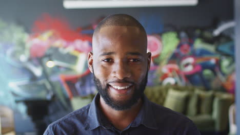 Millennial-black-male-creative-smiling-to-camera-in-front-of-mural,-head-and-shoulders,-close-up