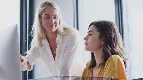 Two-white-female-colleagues-in-discussion-at-a-computer-screen-in-a-creative-office,-close-up