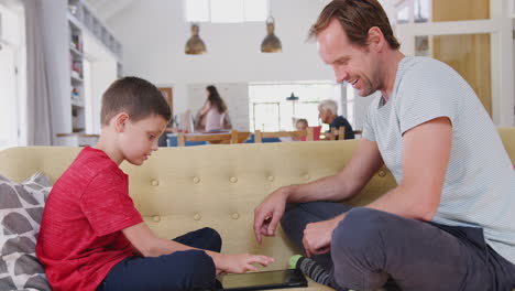 Vater-Sitzt-Mit-Sohn-Auf-Dem-Sofa-Und-Spielt-Zu-Hause-Ein-Spiel-Auf-Einem-Digitalen-Tablet