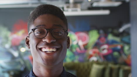 Young-black-man-smiling-to-camera-in-front-of-mural-in-creative-workplace,-close-up,-head-shot
