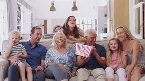 Mehrgenerationenfamilie-Sitzt-Zu-Hause-Auf-Dem-Sofa,-Isst-Popcorn-Und-Schaut-Sich-Gemeinsam-Einen-Film-An