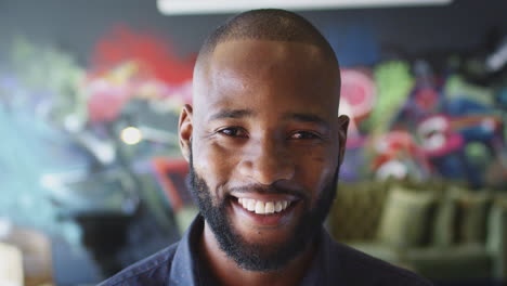 Millennial-black-man-smiling-to-camera-in-front-of-mural-in-workplace,-head-shot