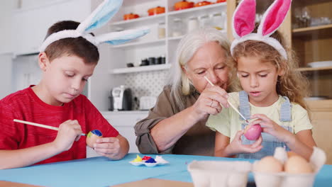 Grandmother-With-Grandchildren-Wearing-Rabbit-Ears-Decorating-Easter-Eggs-At-Home-Together