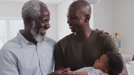 Proud-Grandfather-With-Adult-Son-Cuddling-Baby-Grandson-In-Nursery-At-Home
