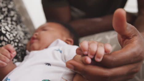 Baby-Son-Gripping-Fathers-Finger-As-He-Cuddles-Him-In-Nursery-At-Home