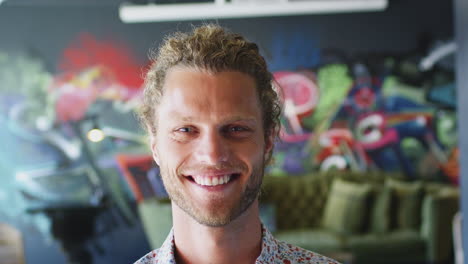 Young-white-man-in-front-of-mural-in-workplace-smiling-to-camera-and-laughing,-head-shot