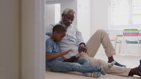Großvater-Sitzt-Mit-Enkel-Im-Kinderzimmer-Und-Nutzt-Gemeinsam-Ein-Digitales-Tablet