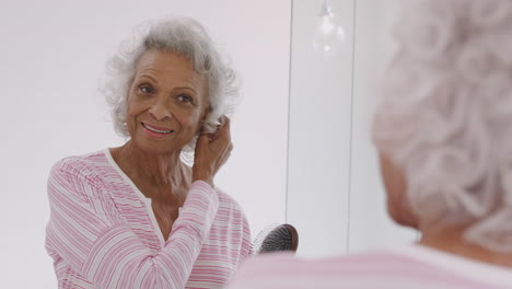 Ältere-Frau-Schaut-Sich-Das-Spiegelbild-Im-Badezimmerspiegel-An-Und-Bürstet-Sich-Die-Haare