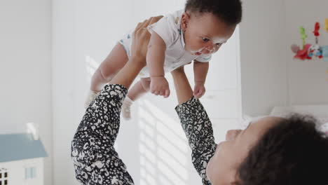 Mother-Cuddling-And-Playing-With-Baby-Son-In-Nursery-At-Home-Lifting-Him-In-Air