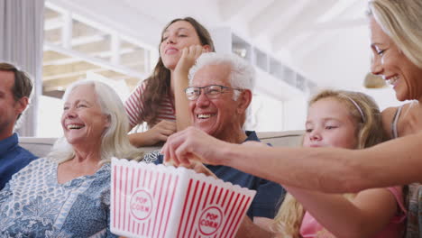 Mehrgenerationenfamilie-Sitzt-Zu-Hause-Auf-Dem-Sofa,-Isst-Popcorn-Und-Schaut-Sich-Gemeinsam-Einen-Film-An