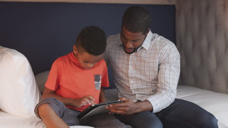 Vater-Und-Sohn-Sitzen-Gemeinsam-Im-Bett-Und-Nutzen-Ein-Digitales-Tablet