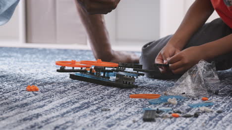 Close-Up-Of-Grandfather-With-Grandson-Sitting-On-Rug-At-Home-Building-Model-Helicopter-Together
