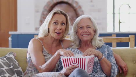 Mutter-Und-Erwachsene-Tochter-Essen-Popcorn-Und-Schauen-Gemeinsam-Auf-Dem-Sofa-Einen-Film