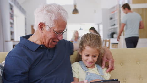 Großvater-Sitzt-Mit-Enkelin-Auf-Dem-Sofa-Und-Nutzt-Zu-Hause-Ein-Digitales-Tablet