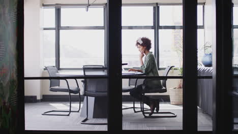 Young-black-businesswoman-working-alone-in-an-office,-seen-through-glass-wall,-full-length,-zoom-out