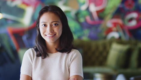 Junge-Kreative-Asiatische-Frau-Lächelt-In-Die-Kamera-Vor-Einem-Wandgemälde-Am-Arbeitsplatz,-Mit-Kopf-Und-Schultern