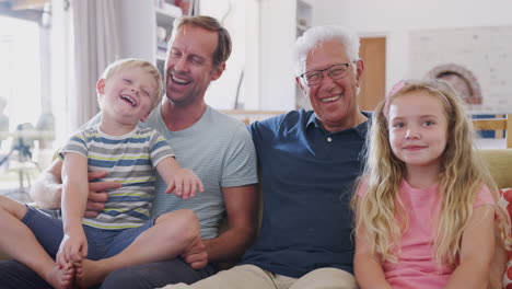 Großvater-Sitzt-Mit-Enkelkindern-Und-Erwachsenem-Sohn-Auf-Dem-Sofa-Und-Redet-Und-Lacht